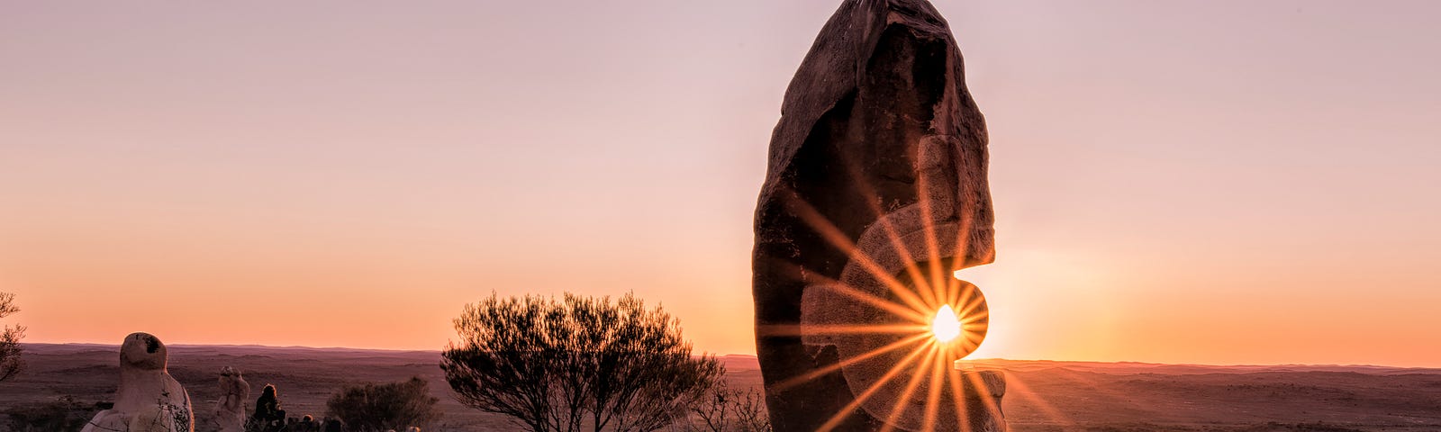 The sun’s healing energy shines through a rock in a desolate desert landscape.