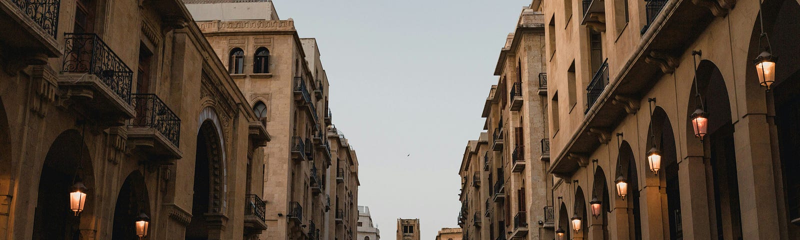 A deserted city street at dusk with all of the lanterns lit.