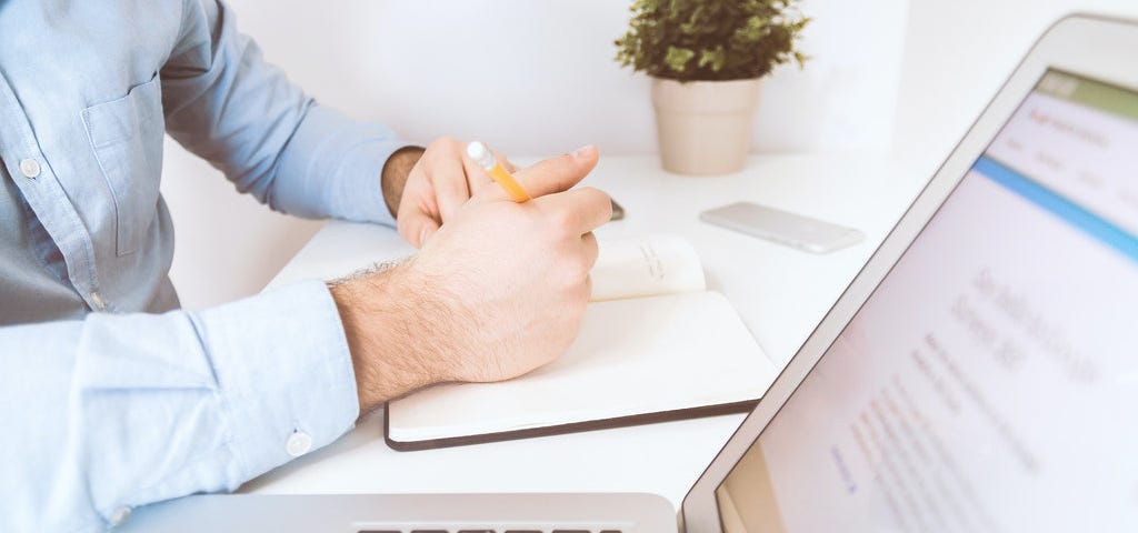 a laptop on a table with hands of a man on the side.