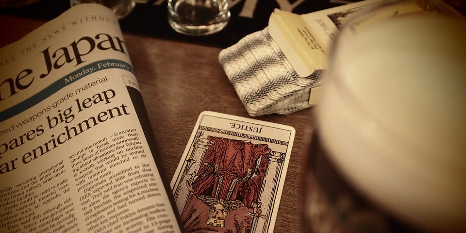 The “Justice” Tarot card, upside down on table with newspaper and the packaged deck it came from