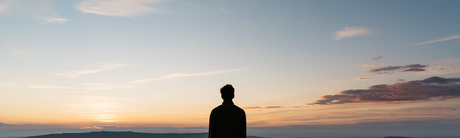 Young man standing and looking at sunset over a horizon