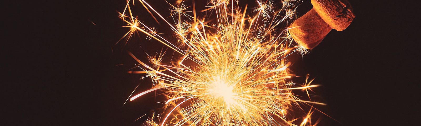 A hand holding a bottle of champagne with fireworks coming out of the bottle.