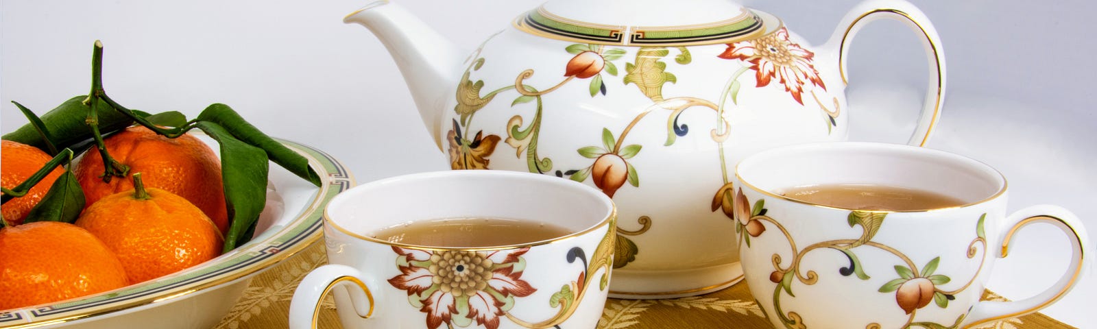 Teapot two teacups bowl of orange fruit