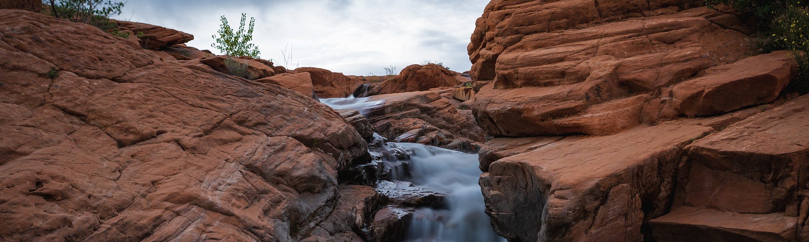 View of Gunlock Falls with water flowing between bright red rocks.