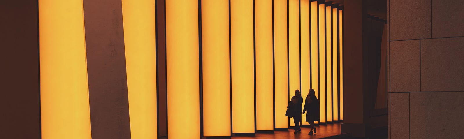 two silhouettes of people walk in a hallway of tall doors