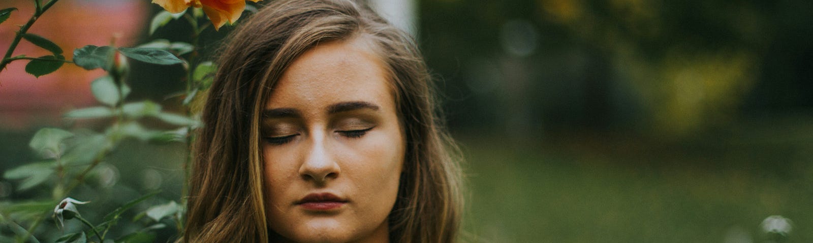 Woman by rosebush with eyes closed.