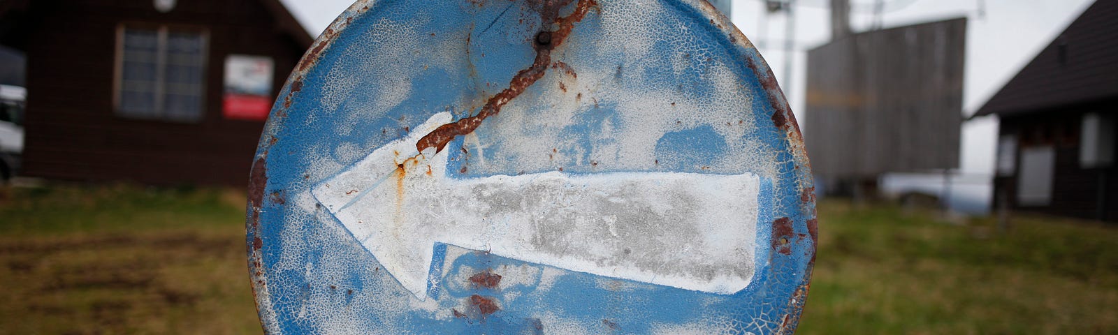 Round rusted blue sign with a painted white arrow pointing left.