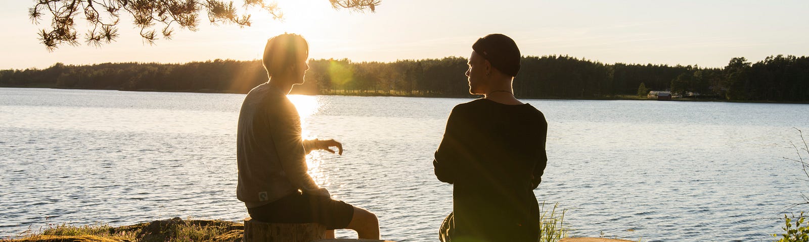 Two men sitting by a lake talking.