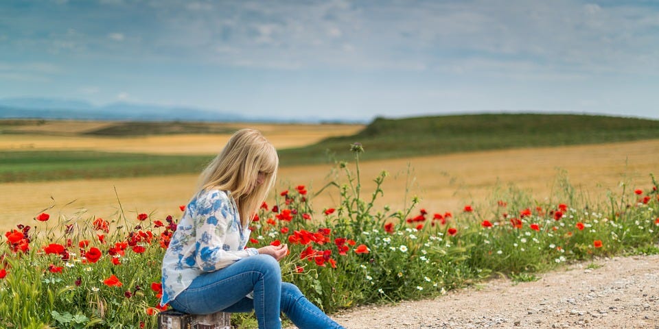 Girl waiting at side of the road sitting on a suitcase.