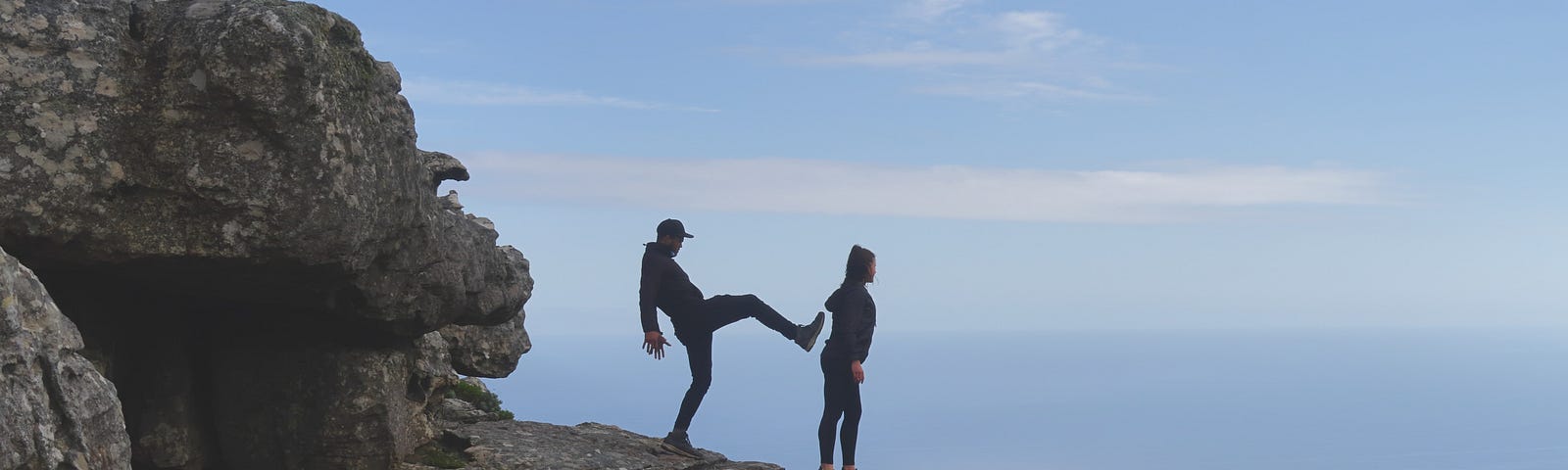 A man aims a kick at another’s back on the edge of a cliff.