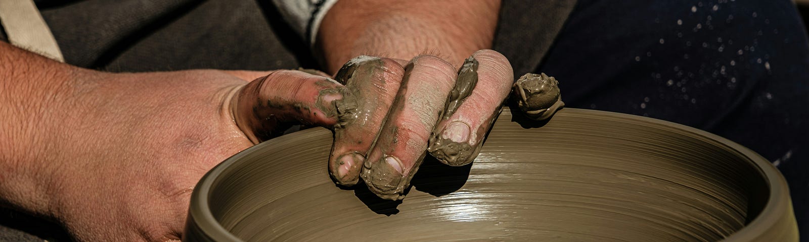 Male hands molding a pot on a potter’s wheel.