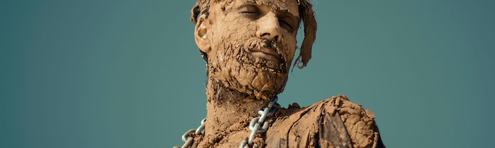 A man covered in clay and wearing a chain.