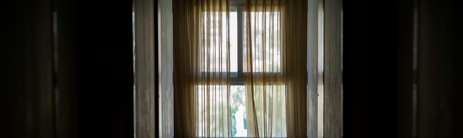 A curtained window at the end of a darkened hallway