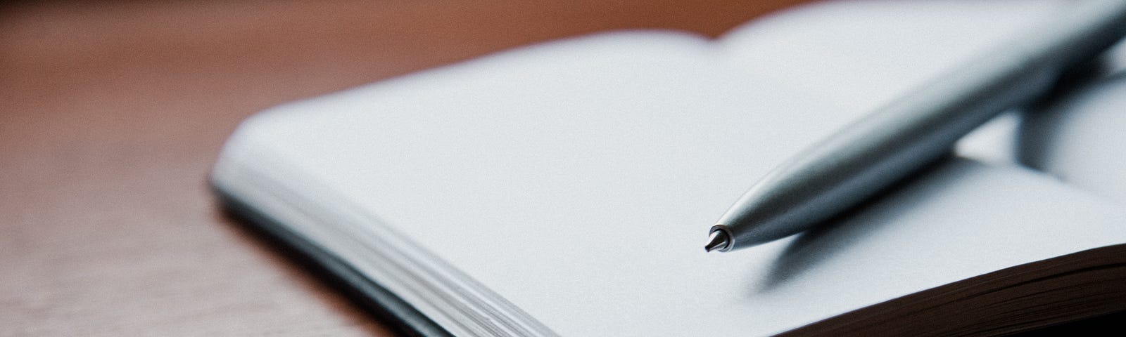 Picture of a desk with an open notebook and a pen.