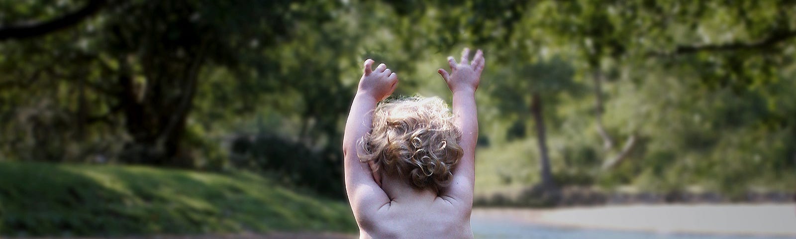 A toddler stands in a shallow, rural waterway, holding its arms up victoriously.