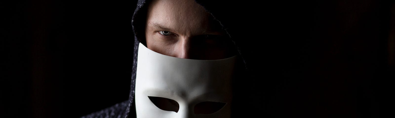 a man in the dark holds up a white mask to cover half his face