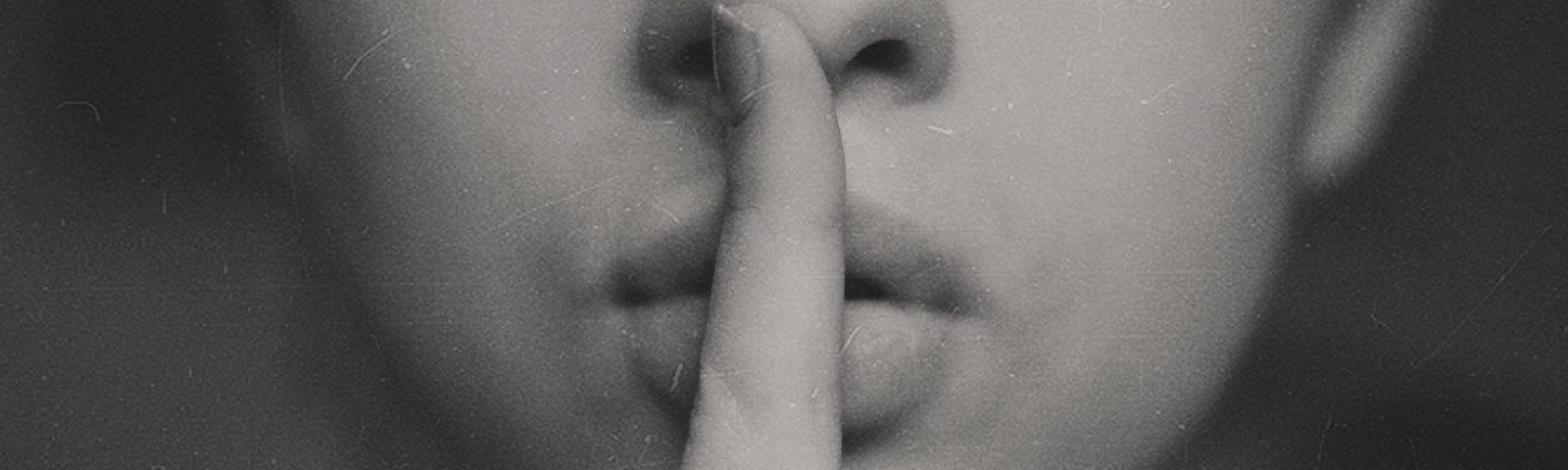 An individual holds a single index finger in front of their lips, in a “hushing” gesture.