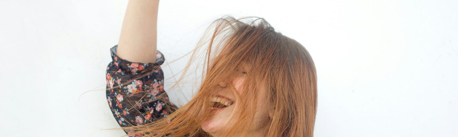 A woman with long, red hair smiles gleefully. One hand is raised in the air as her hair blows in the wind. She appears to be carefree.