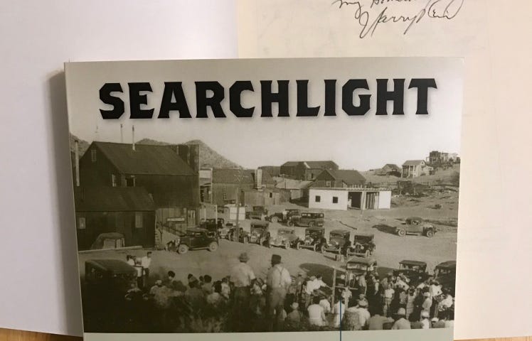 Photograph of the book “Searchlight: The Camp That Didn’t Fail” by Harry Reid. It is holding open a second book of the same name on the title page “Searchlight” inscribed “To Joyce — my Hometown — Harry Reid.”