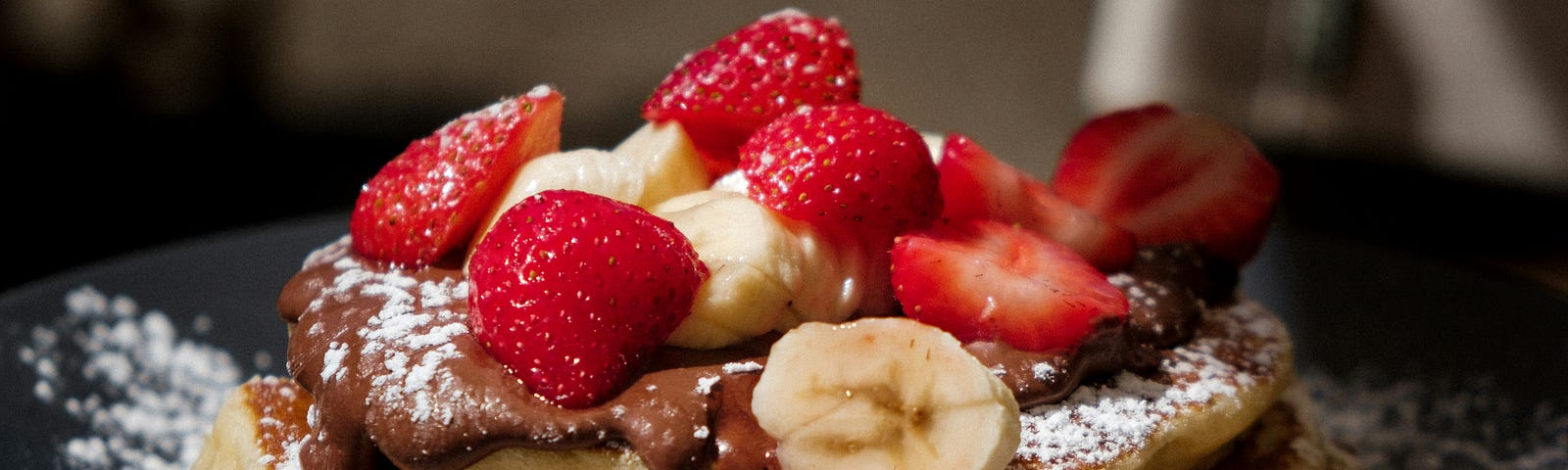 A large stock of pancakes topped with strawberries, bananas and chocolate sauce — yum!