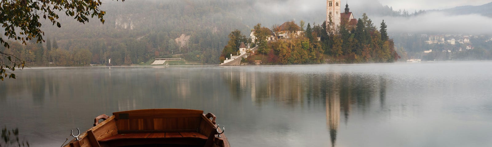 A photo of a boat near the end of a pier on a lake. An island with a castle is visible across the body of water.