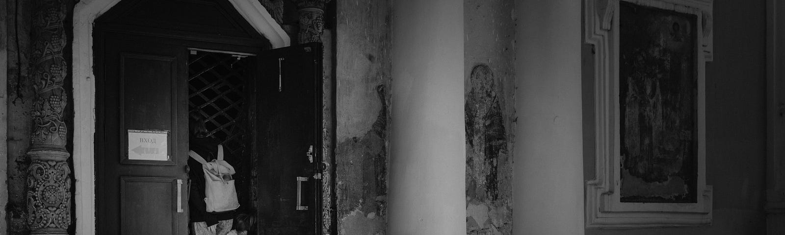 An adult and child peer through a grating at the door of an old church with faded fresco paintings, suggesting a bewildered, frustrated curiosity at the cultural artefacts within