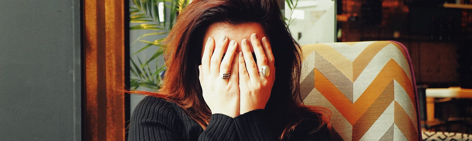 Woman sitting on a chair and holding her hands over her face in pain