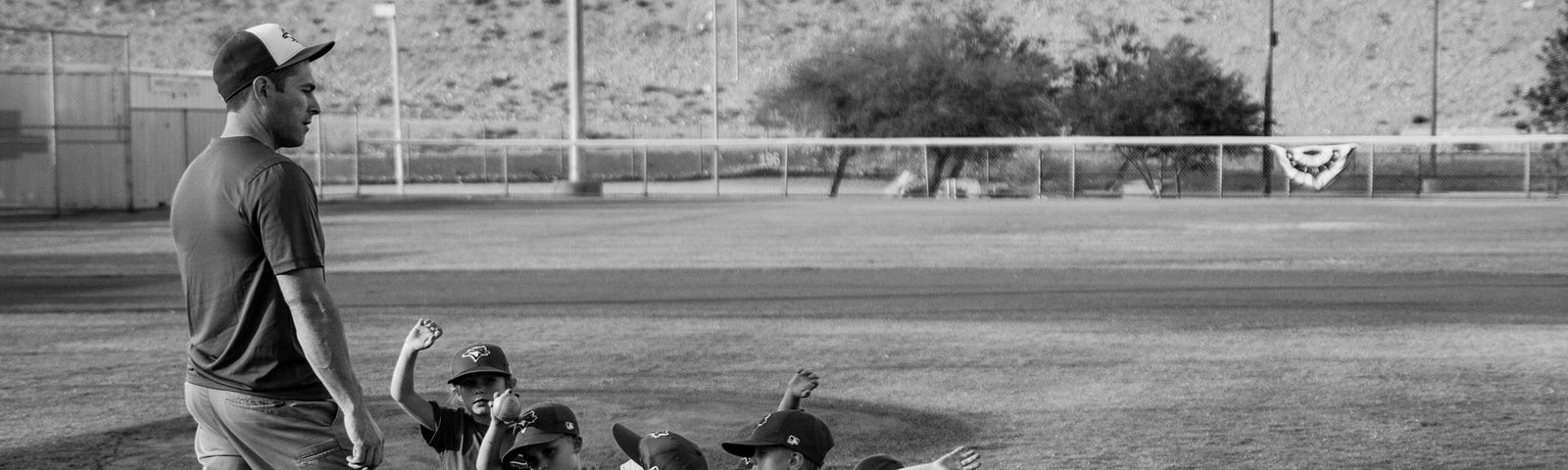 A little league baseball coach is standing over his team on a baseball field