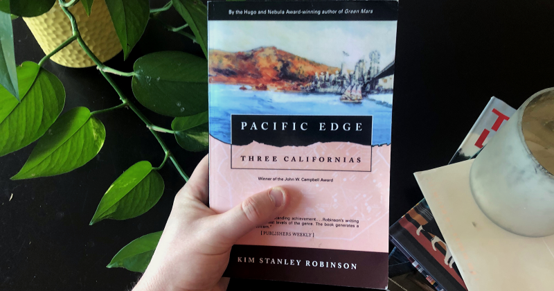 Photo of a man holding Pacific Edge by Kim Stanley Robinson.