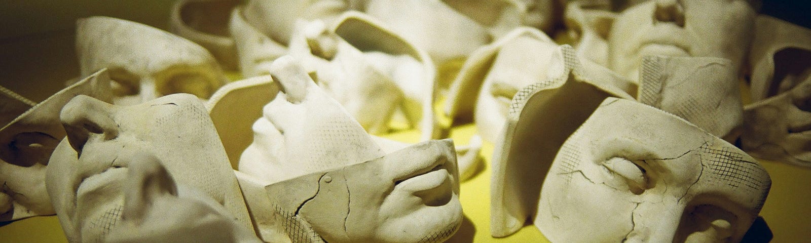 a yellow surface is covered in broken masks made of clay or stone