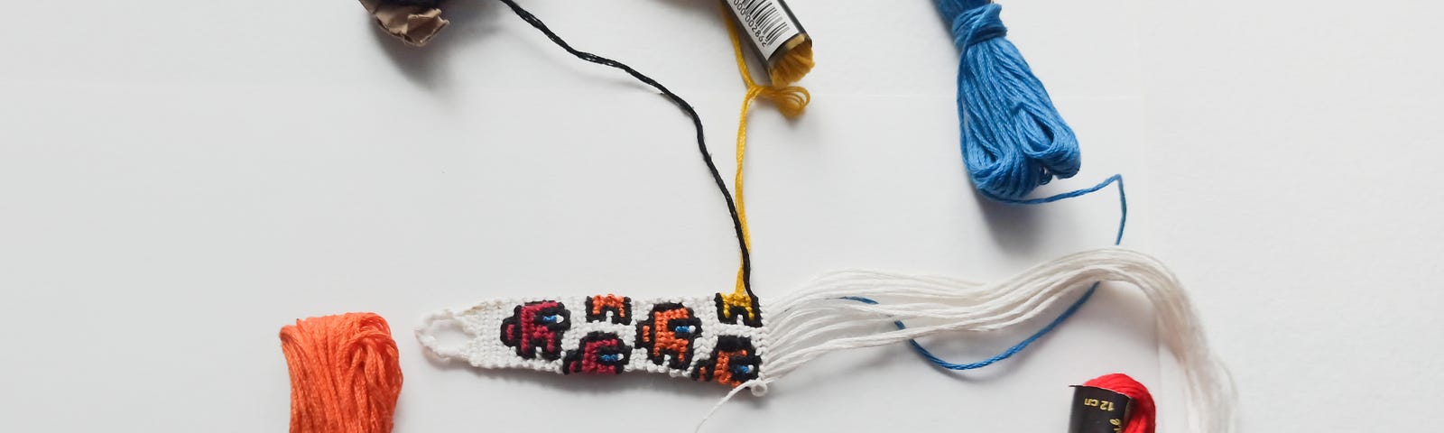 A hand knotted bracelet in progress, with different colored cords on white background
