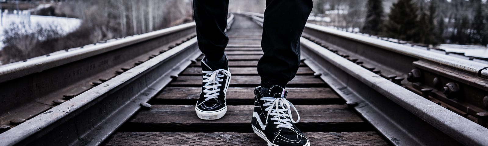 A teenager’s legs and tennis shoes as they cross a railroad bridge during the winter
