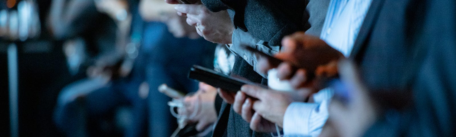 Close up photo of the hands of multiple people standing together, a cell phone in each pair of hands.