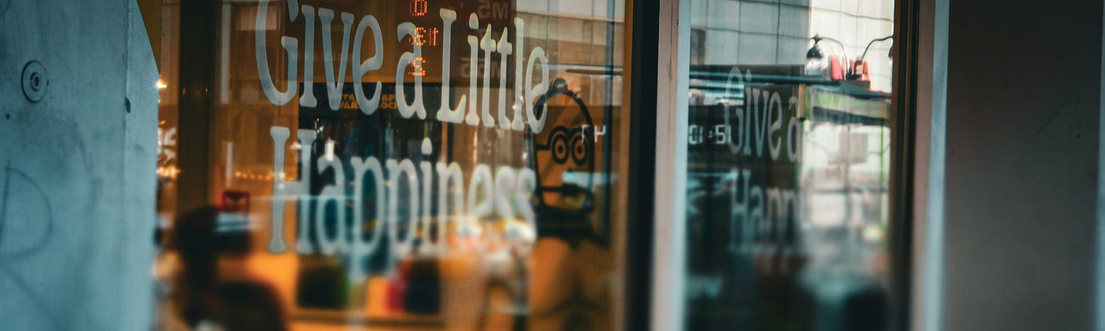 A storefront with the words “Give a Little Happiness” on the window