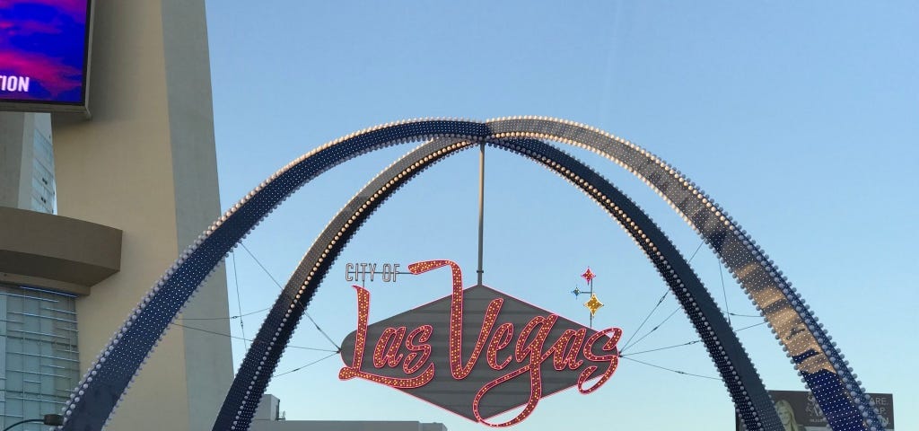 Photo of Las Vegas sign in red lights in downtown Las Vegas with buildings in the background.