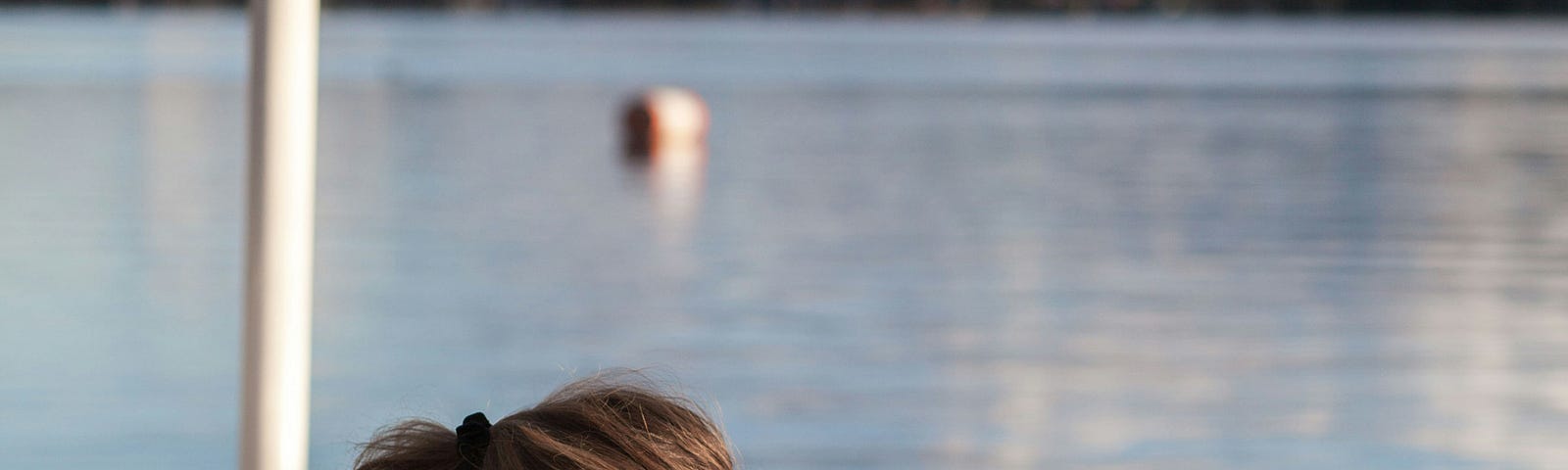 A girl reading on a pier. She has long brown hair with blond highlights.