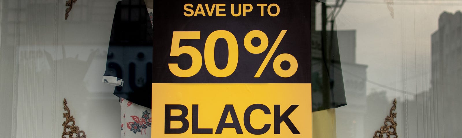 A black and yellow sign posted in the window of a store that says “Save up to 50% Black Friday Now it’s time to save big”