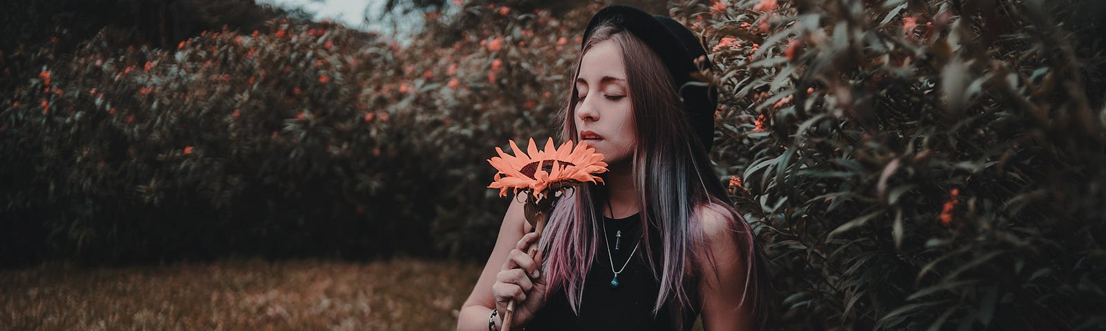 Female sat on ground and smelling a flower