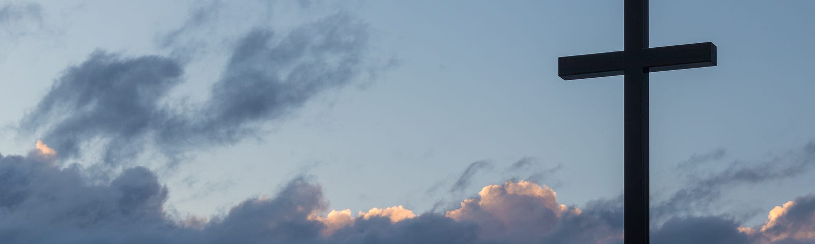 A tall cross amidst a blue slightly cloudy sky.