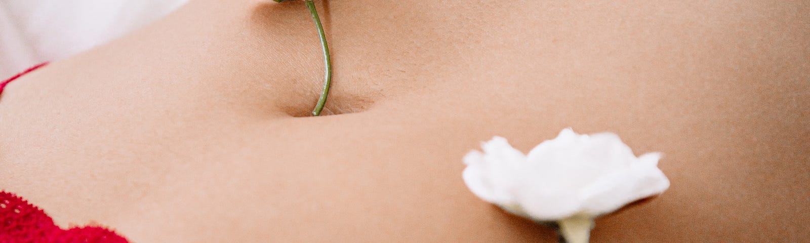 The torso of a woman lying on a bed wearing read bra and panties. Her stomanch has some small flowers scattered across it.