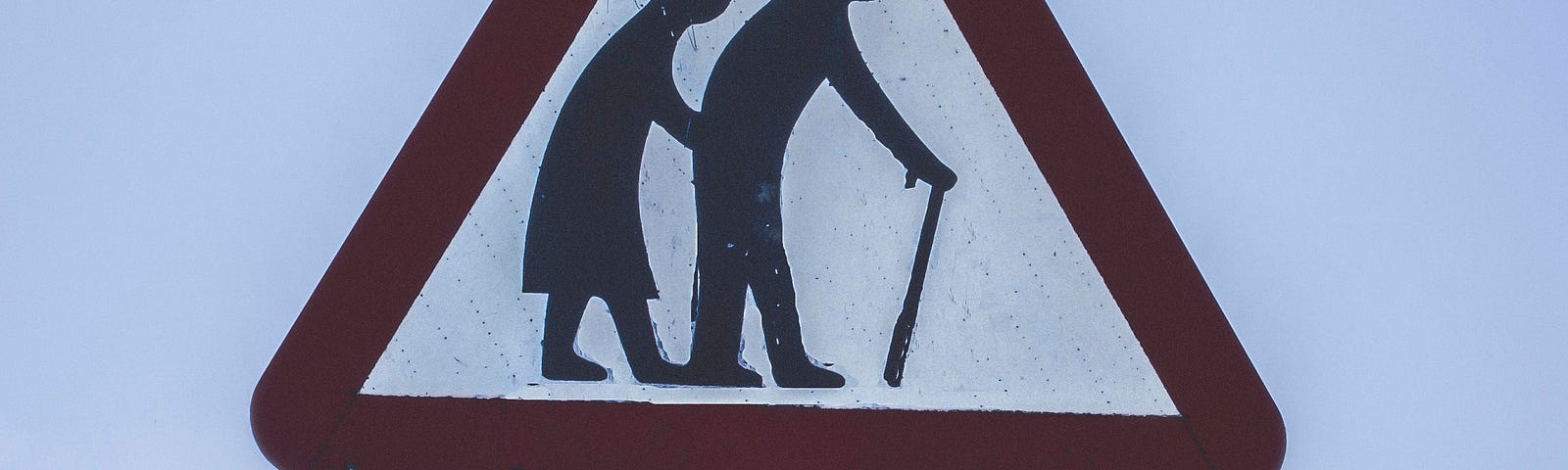 A triangular street sign depicting 2 elderly people over another sign that says “Elderly People”