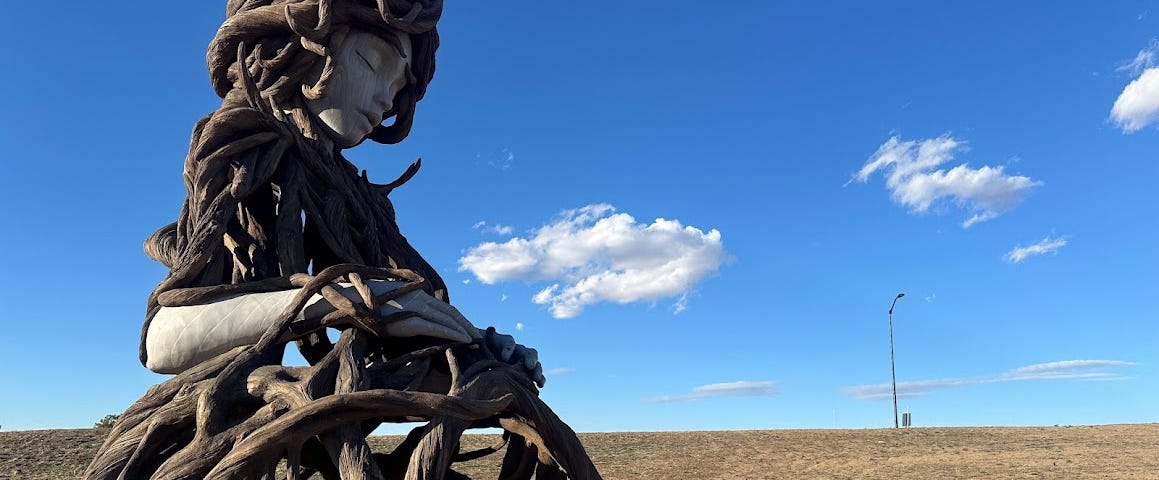 Umi Statue by Daniel Popper located in Aurora Colorado. Shows a woman with eyes closed made out of tree roots as though she’s growing out of the Earth.