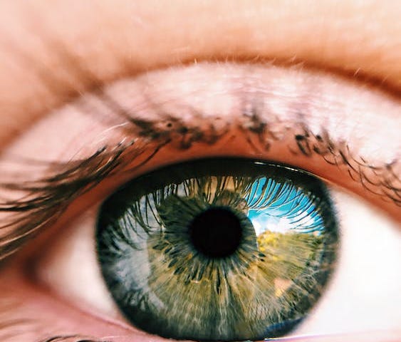 Close-up of a human eye. You can see a mountainous landscape and blue sky with clouds reflected in the eye.