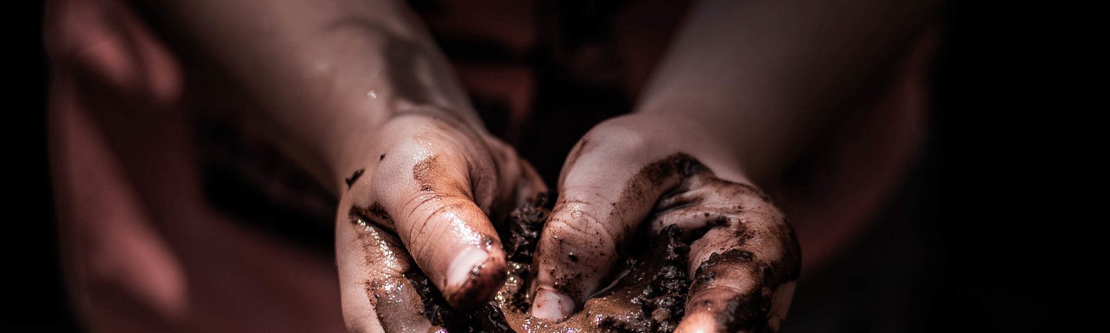 close up of child’s hand holding mud and making heart shape