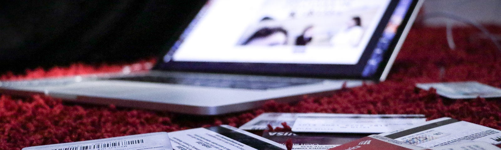 A laptop is placed on a red carpet surrounded by credit cards.