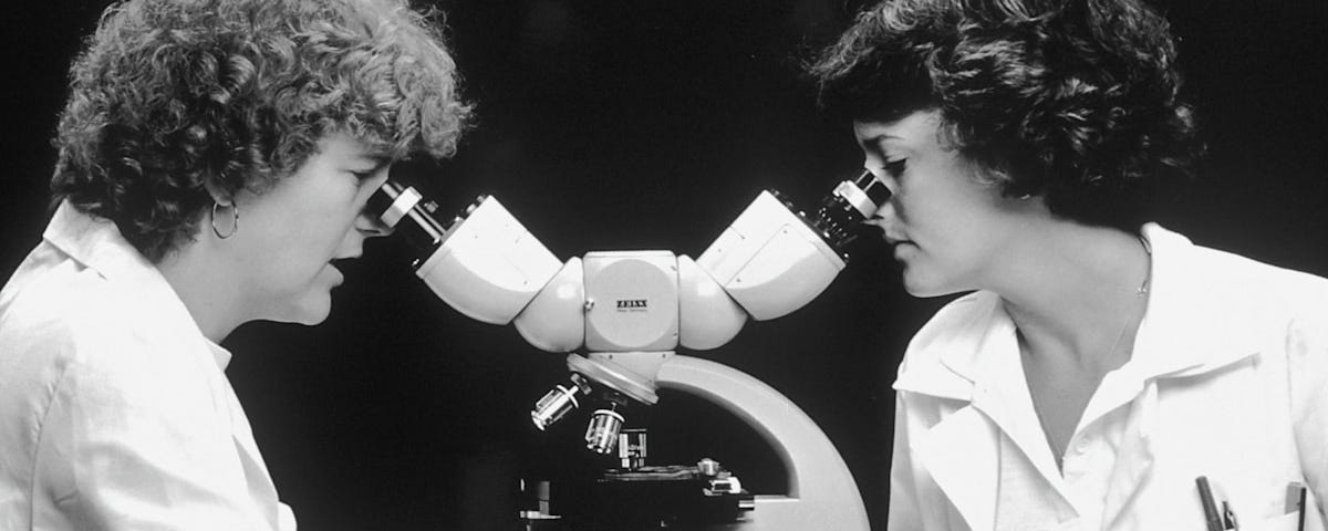 Two scientists looking into the same microscope