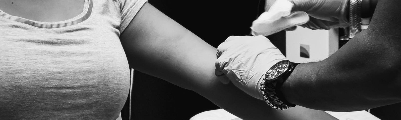 torso of woman getting blood drawn from her arm by a person wearing latex gloves