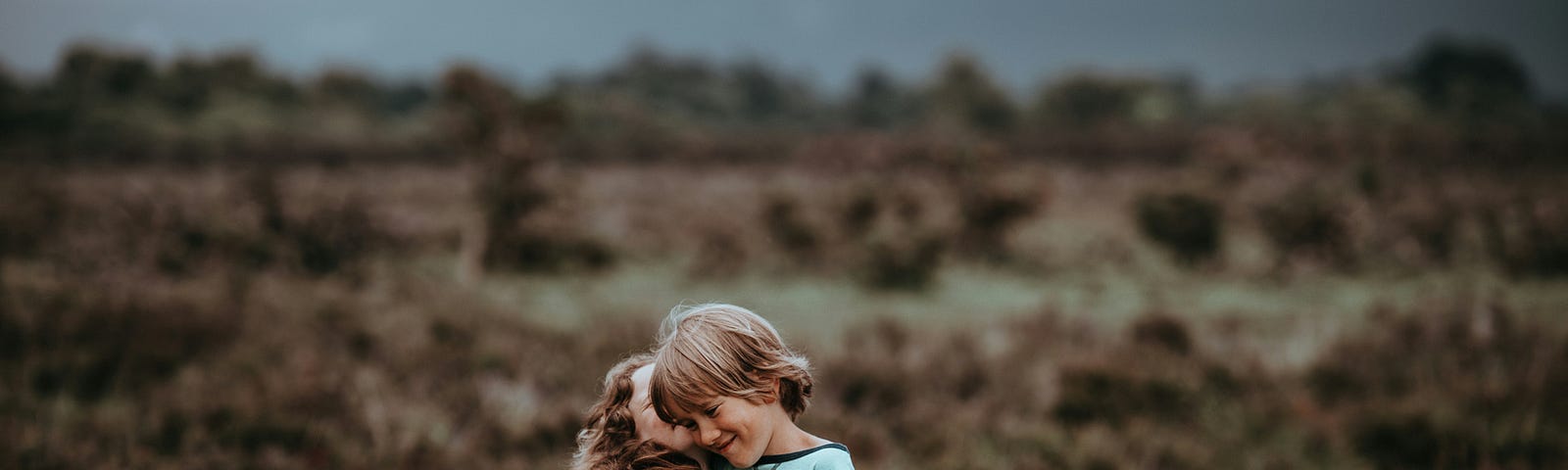 Two child friends hugging each other in the middle of a grassfield.