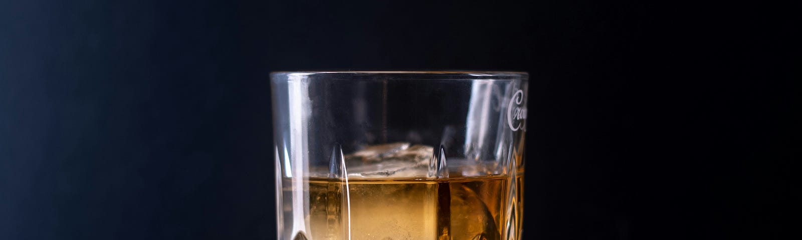 A glass of amber-colored scotch or whiskey sits on a reflective surface against a dark background. The liquor catches the light, revealing its transparent yet enticing nature, setting an ambiguous and somewhat ominous tone.