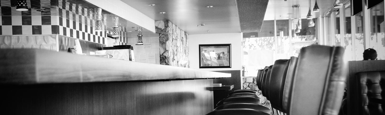 Black and white photo of the seats and counter at an American diner.